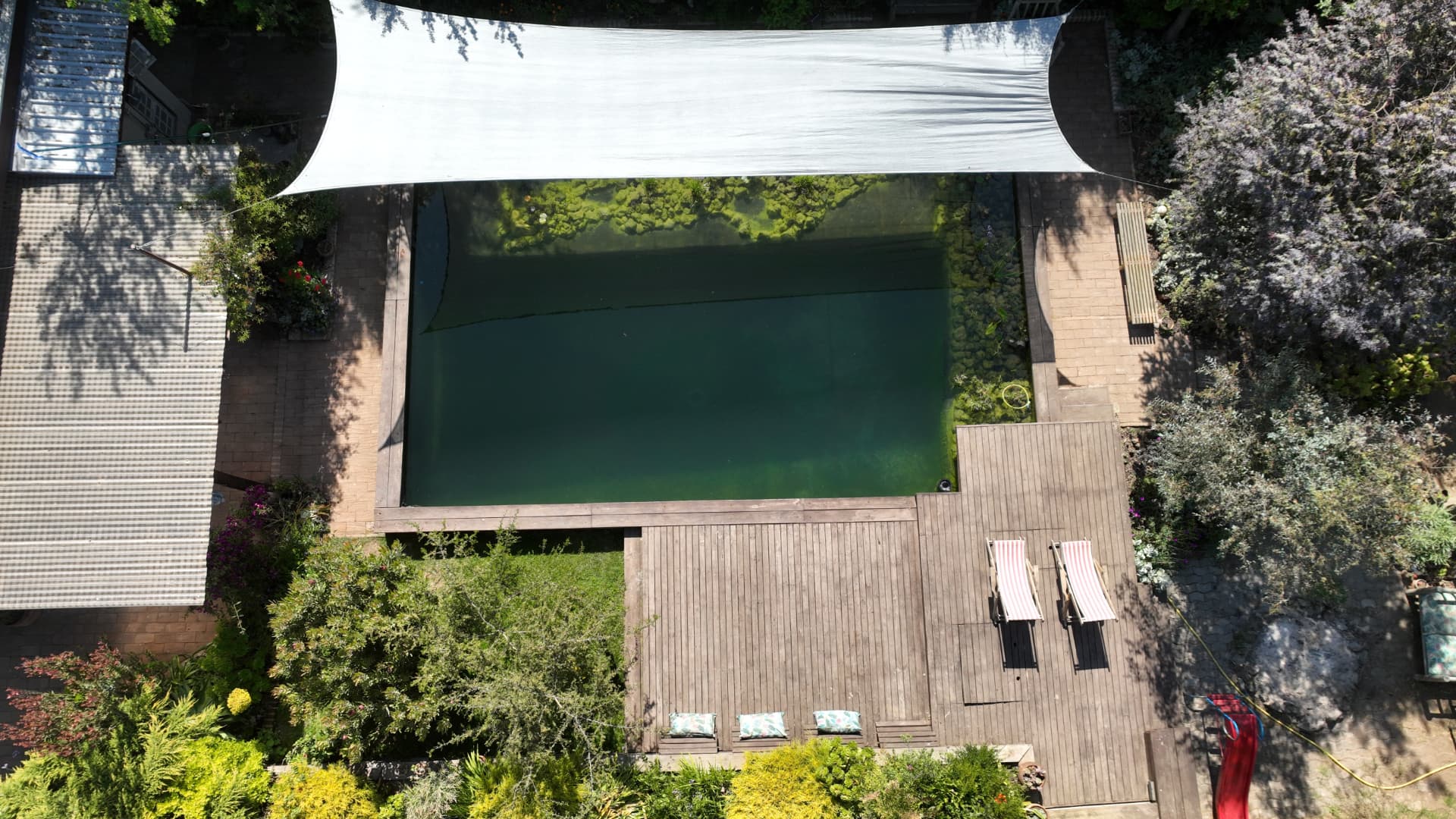 Vista aérea de la biopiscina con toldo blanco, terraza con tumbonas y piedra